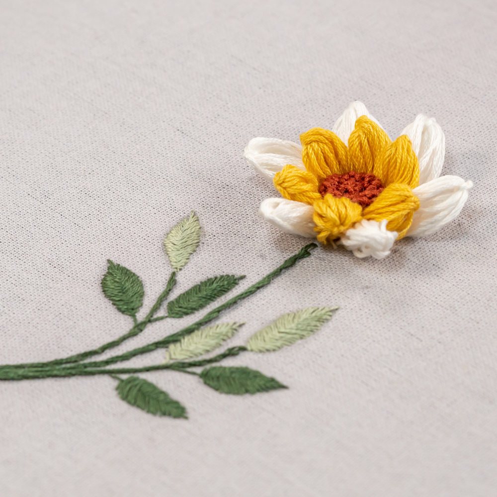 detail of embroidered flower with white petals and green leaves